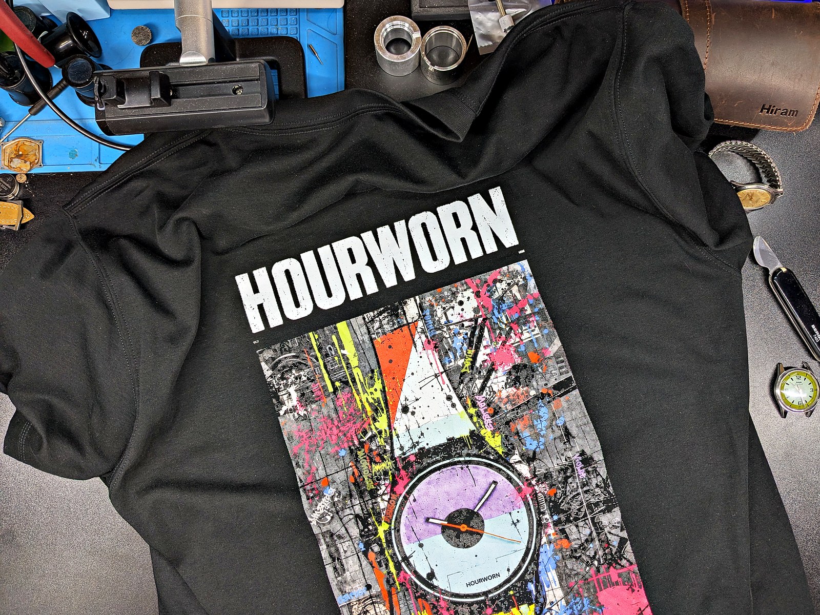 The first printed Hourworn sample, the 80s Graffiti T-shirt in black, laid out on Jeff’s watch repair bench among tools and watches